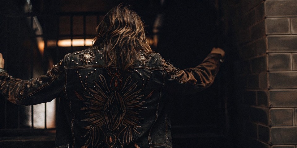 A denim jacket with a vibrant mix of customizations: a large embroidered back piece, some patches on the sleeve, and custom buttons.