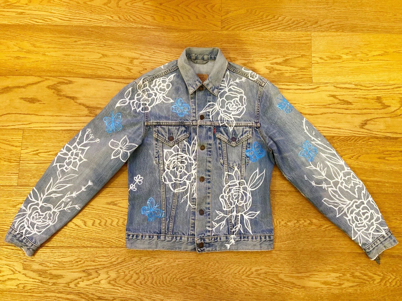 The Front of the Customised jacket has white flowers spaced irregularly all over the jacket with pretty blue butterflies flying all through the jacket. The sleeves have graduated painted flowers, so they are heavier from the sleeve and into almost n…